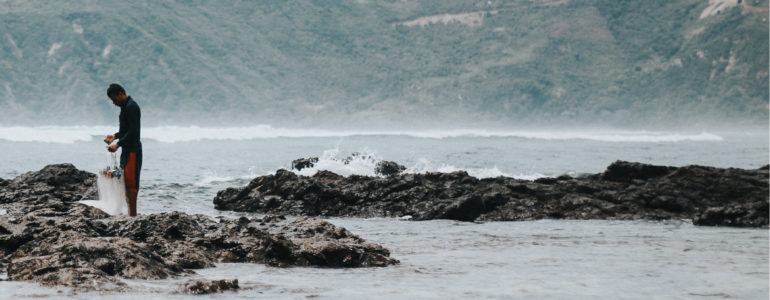 a person stands near a wave crashing on a rock
