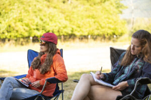 Two students taking notes while sitting in front of a river. 