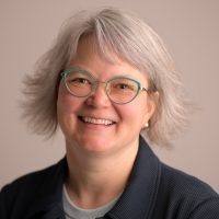 headshot of smiling woman with silver hair and green glasses